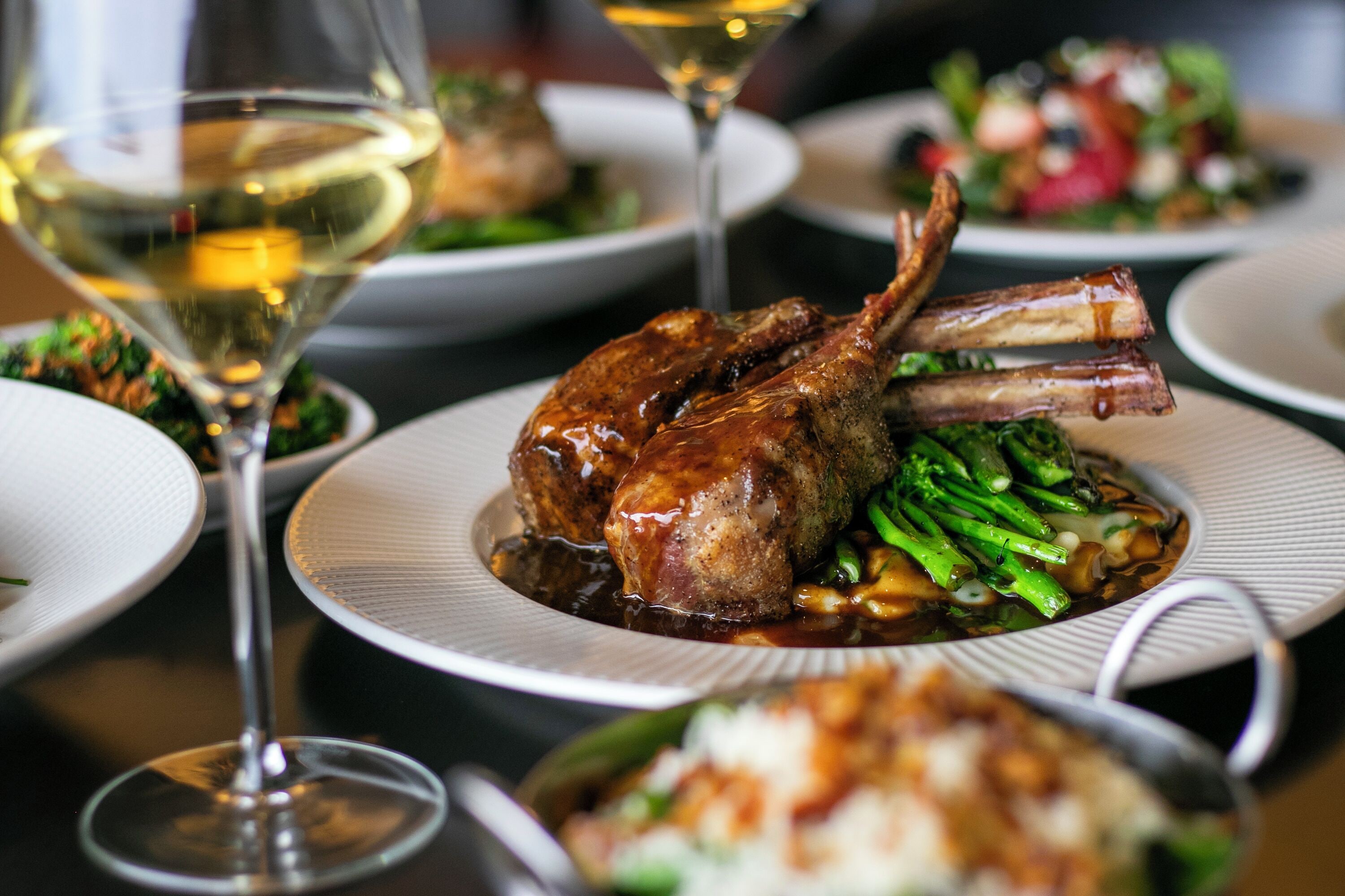 A dining table with plates of food, including a roasted duck and green vegetables, and wine glasses.