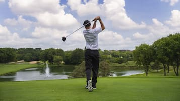 A golf course with a pond, trees, and a clear sky.