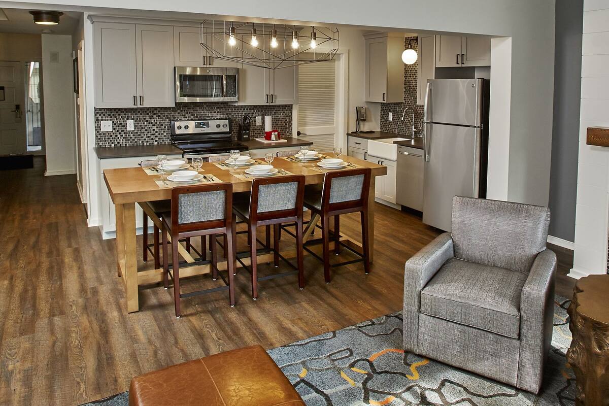 A modern kitchen with a dining area, wooden flooring, and a staircase leading to an upper level.