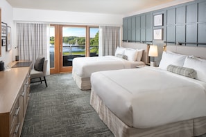 A hotel room with two beds, a desk, and a view of a lake.