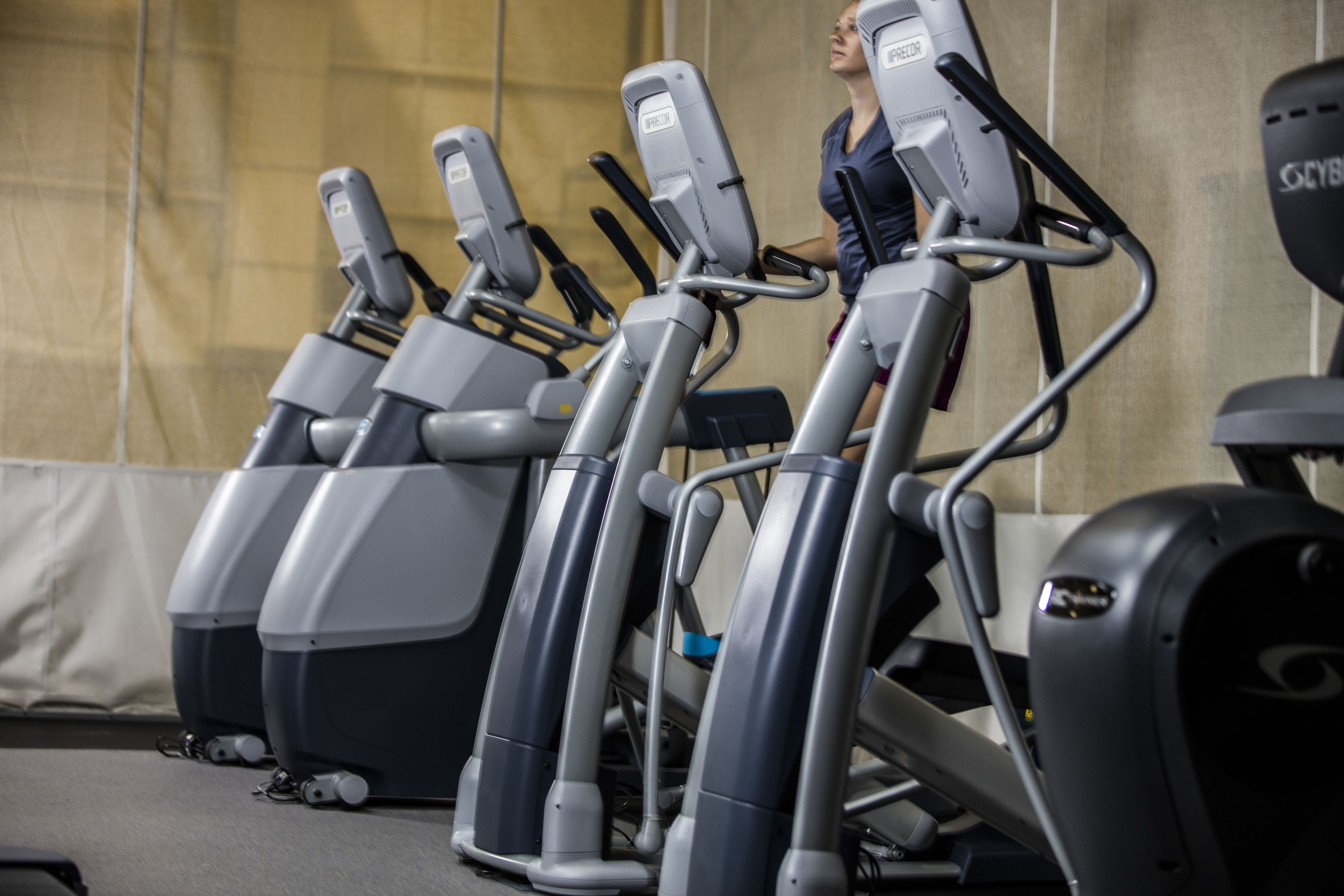 A row of stationary bikes in a gym with a plain wall in the background.