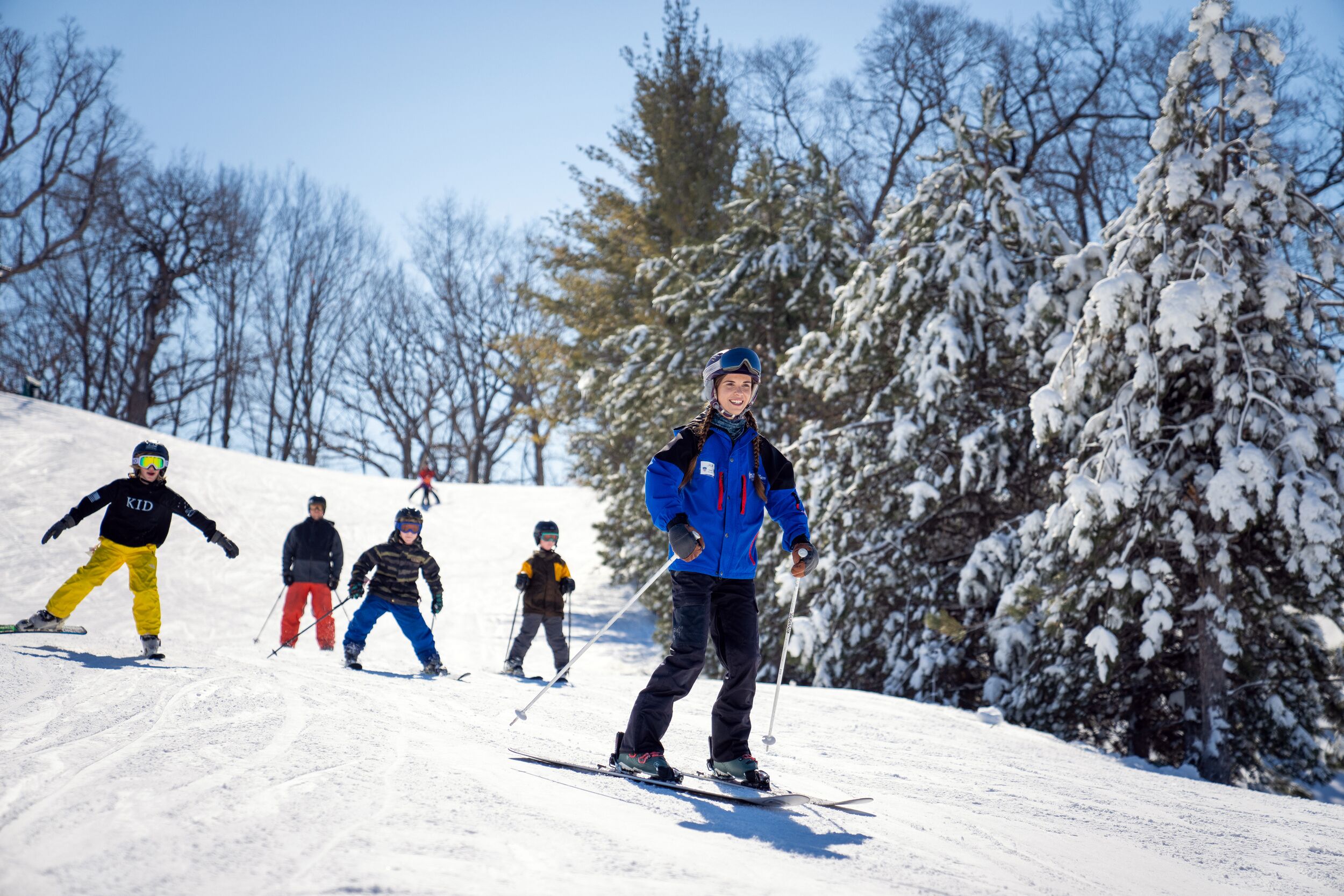 A group of skiers on a snowy slope with trees in the background.