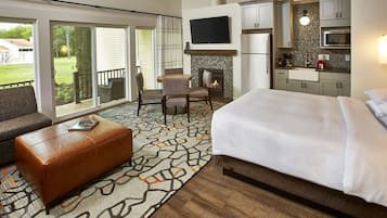 Quarto de hotel com cama, sofá, mesa de centro, lareira, televisão e cozinha.