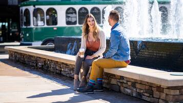 A couple sitting on a stone bench near a fountain, with a green bus in the background.