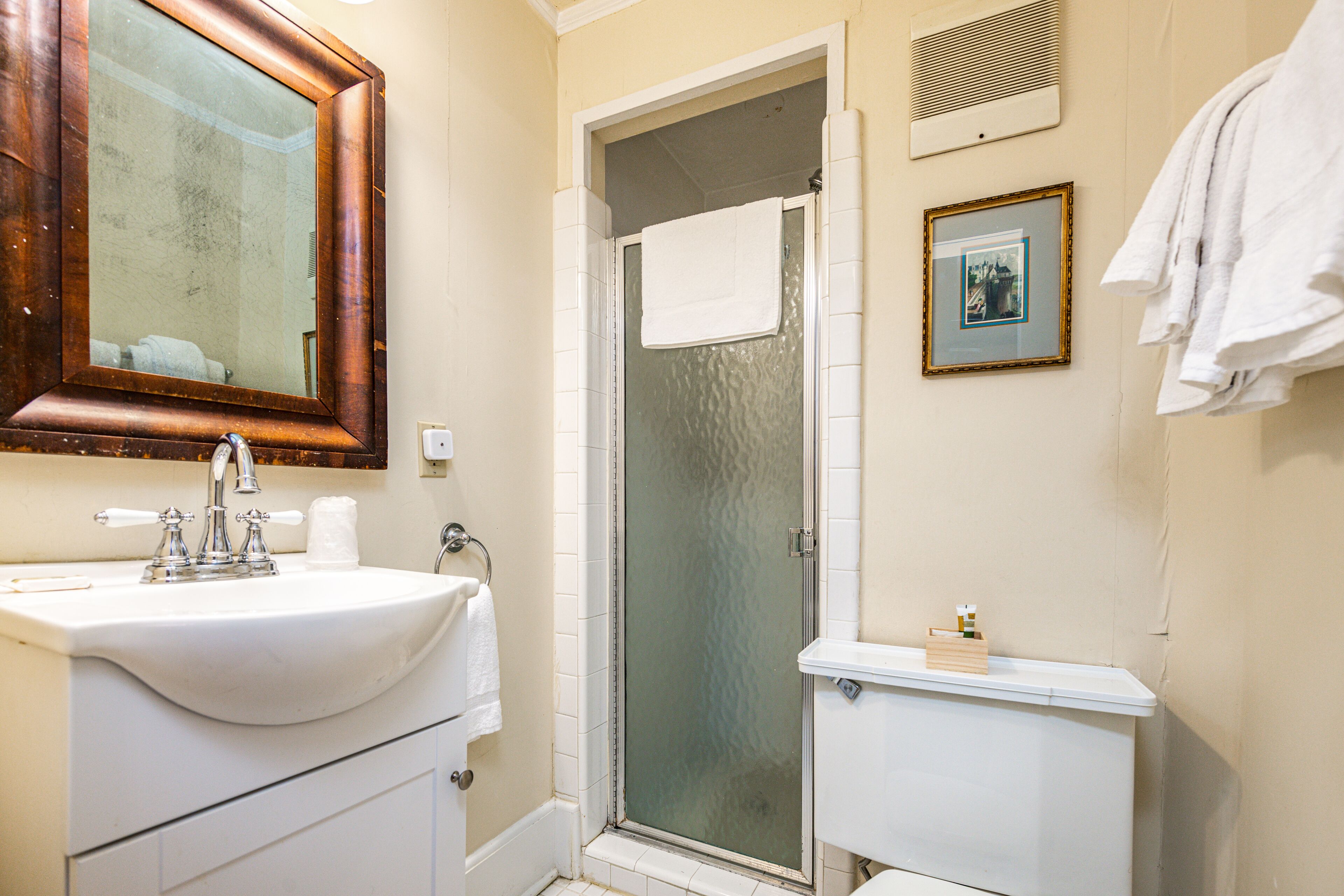 A bathroom with a sink, mirror, shower, toilet, and towel rack.