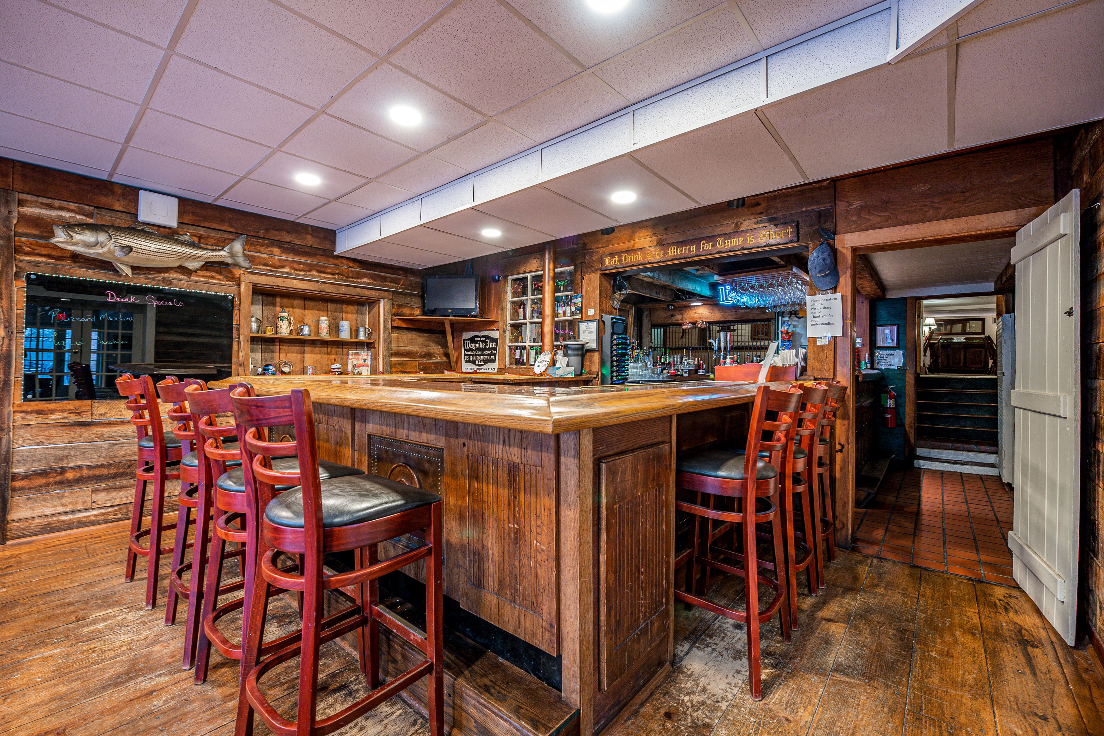 A bar area with wooden bar stools, a wooden counter, and shelves with bottles.
