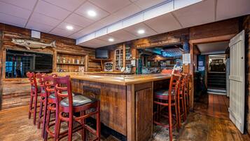 A bar area with wooden bar stools, a wooden counter, and shelves with bottles.