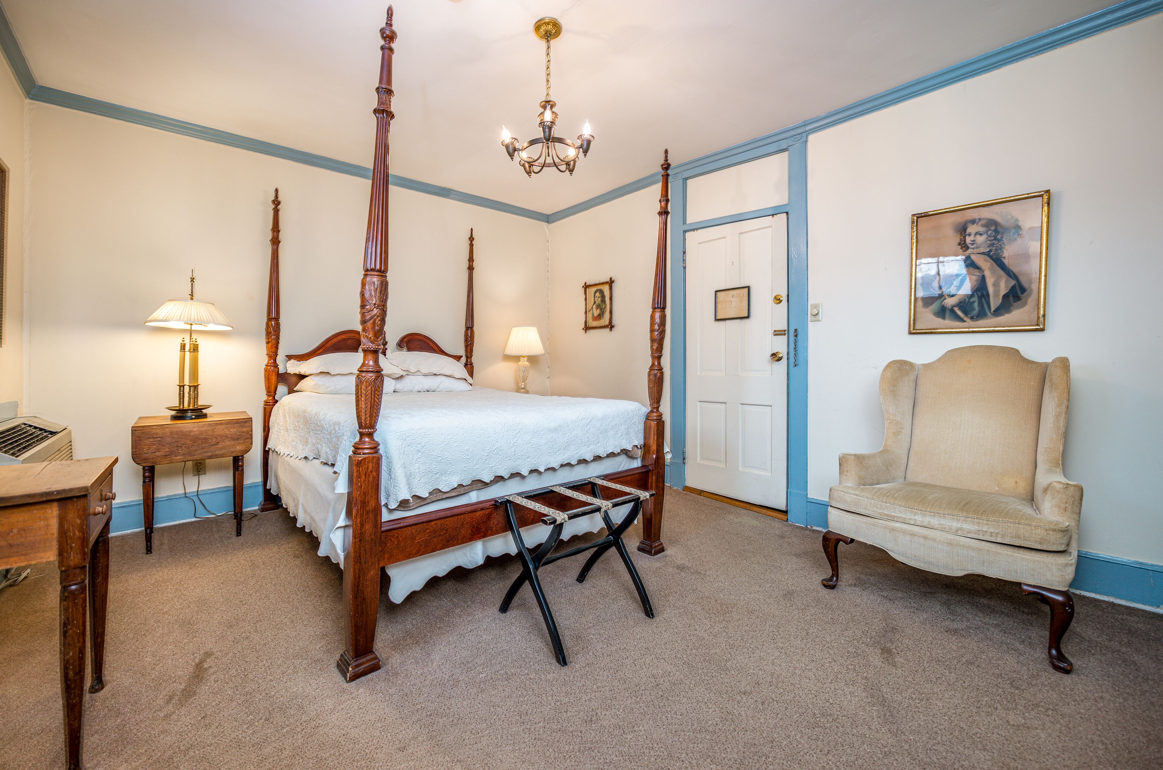 Een slaapkamer met een hemelbed, een houten stoel, een bureau en een kroonluchter.