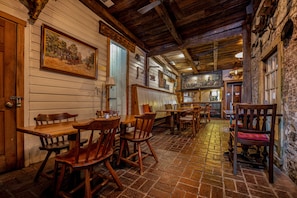 A rustic interior with wooden tables and chairs, a brick floor, and a wooden ceiling.
