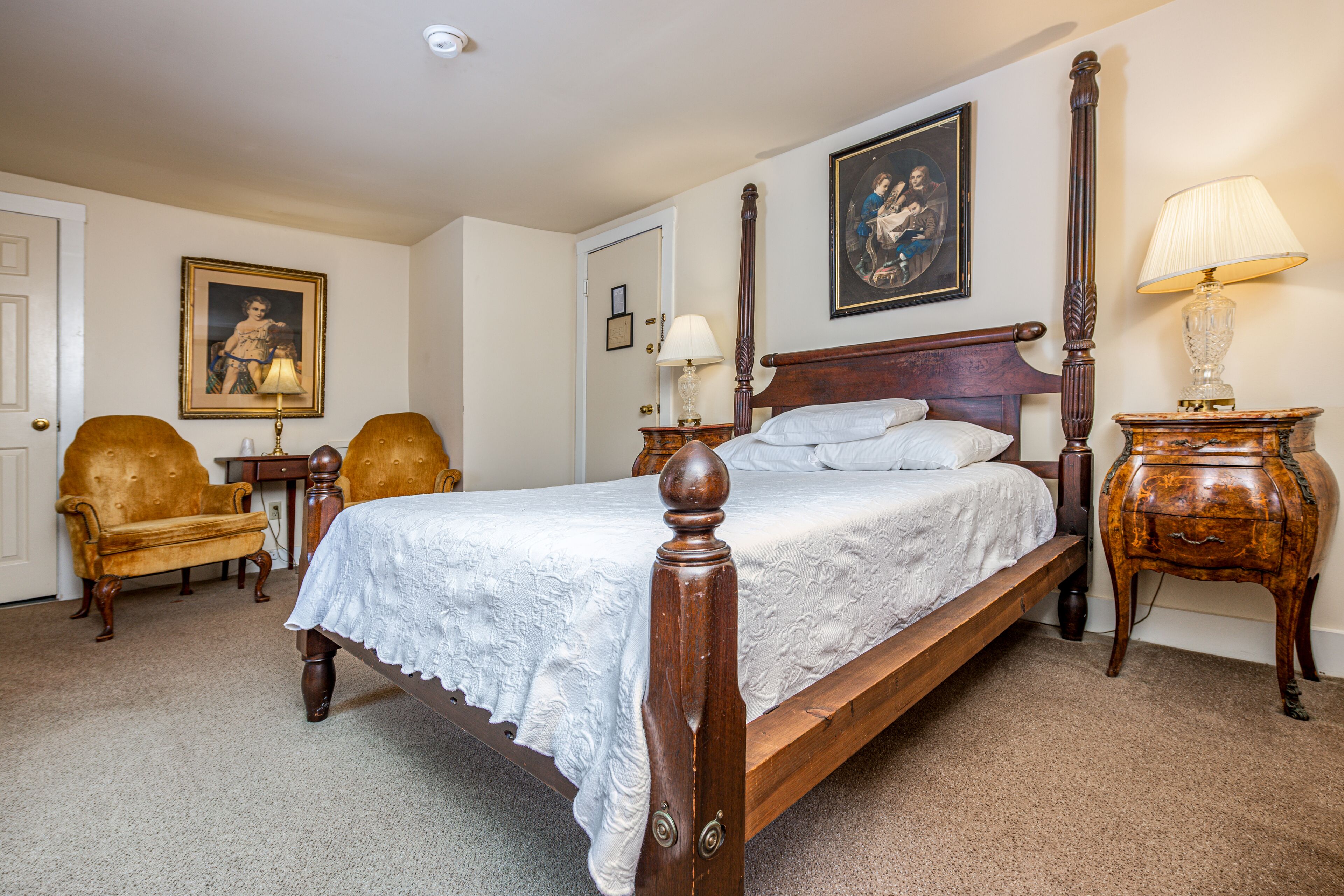 A bedroom with a four-poster bed, a wooden nightstand, a chair, and a lamp.