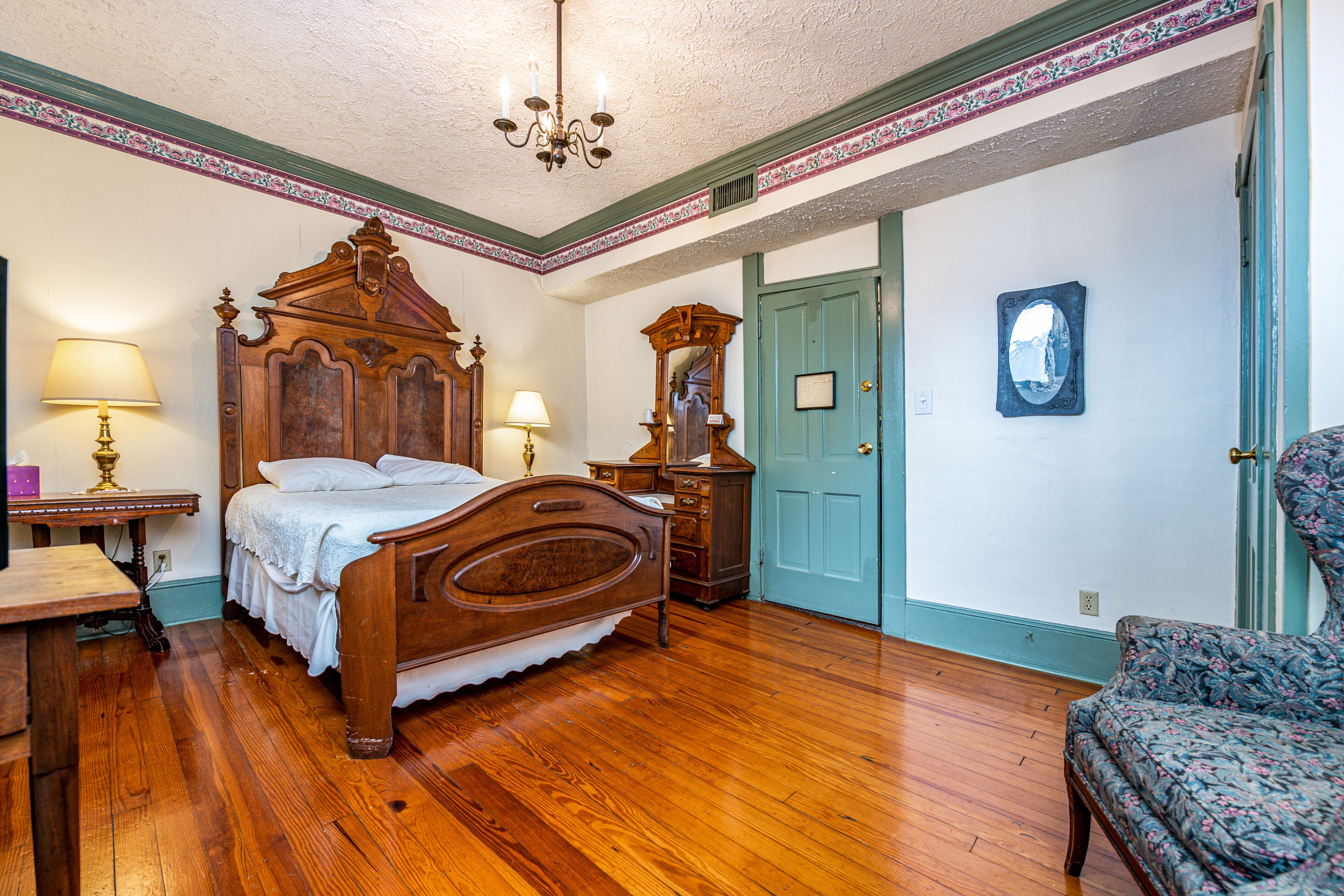 A bedroom with a wooden bed, a dresser, a chair, and a door.