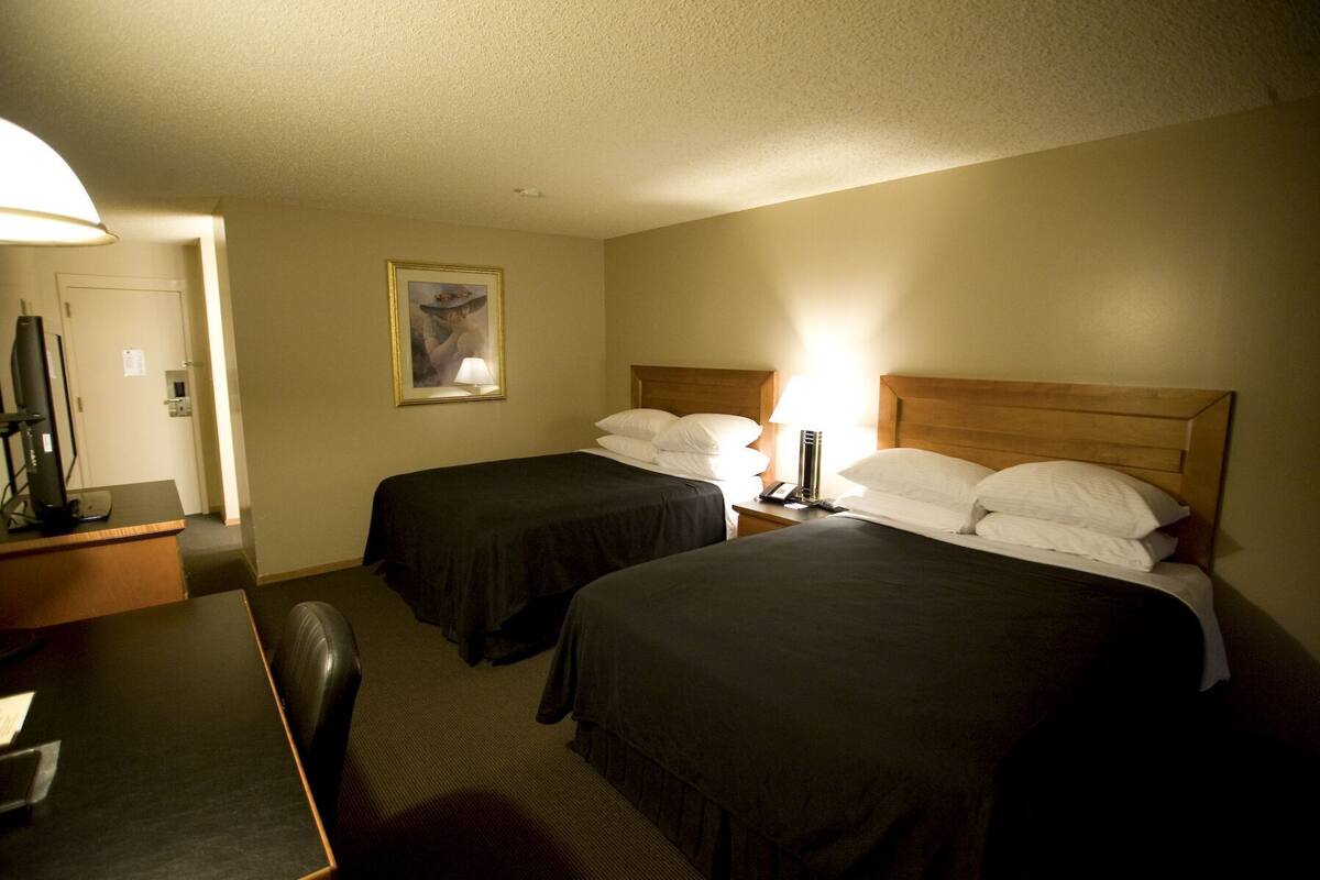 A hotel room with two beds, a desk with a computer, a lamp, and a framed picture on the wall.