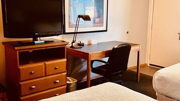 A hotel room with a bed, a desk with a computer, a TV, and a framed picture on the wall.