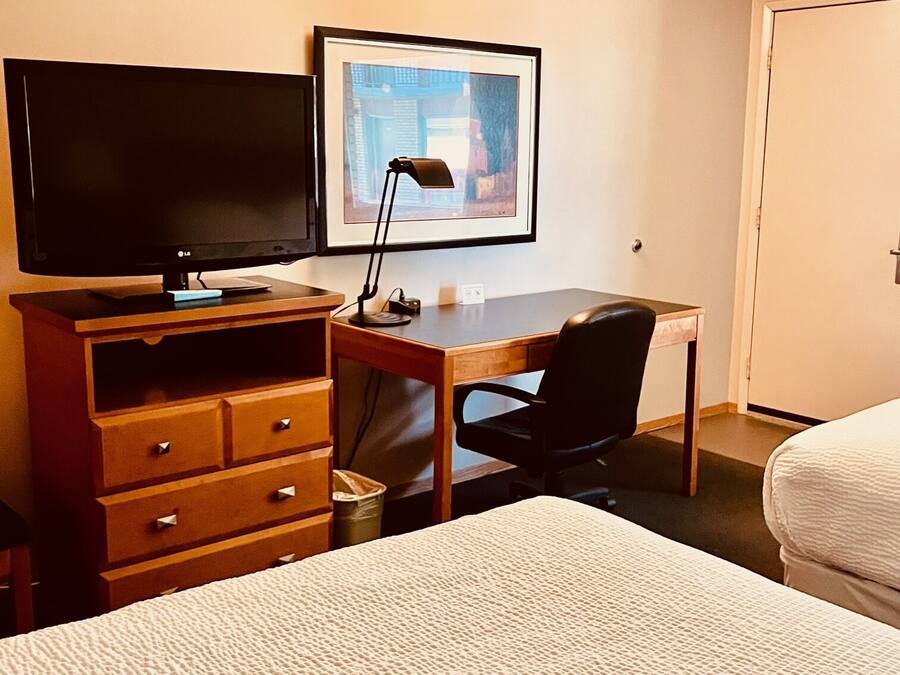 A hotel room with a bed, a desk with a computer, a TV, and a framed picture on the wall.