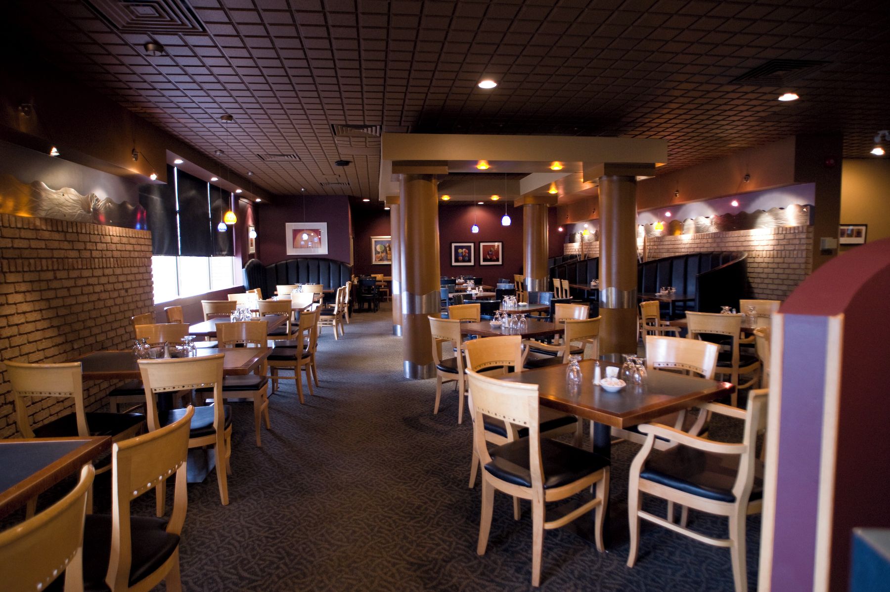 L’intérieur d’un restaurant, avec plusieurs tables et chaises, un tapis à motifs et un mur en briques.
