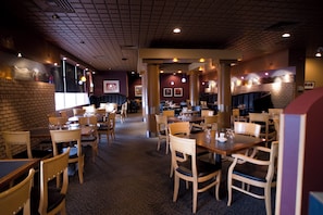 A restaurant interior with multiple dining tables and chairs, a patterned carpet, and a brick wall. - Royal Hotel (Lloydminster)
