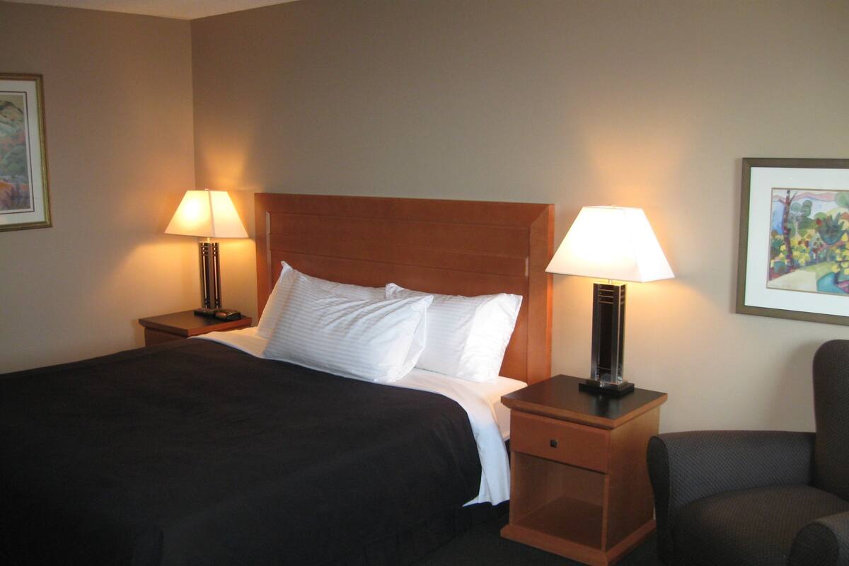 A hotel room with a bed, two bedside tables with lamps, a chair, and artwork on the walls.