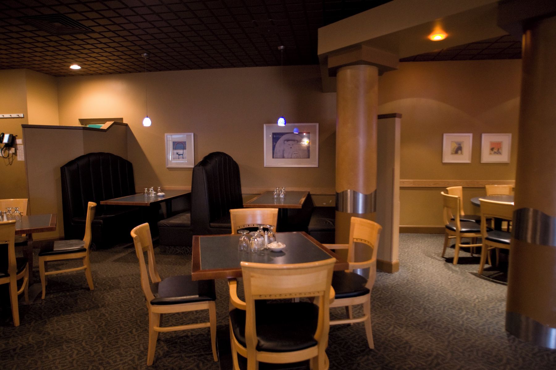 A restaurant with a mix of booth and table seating, a patterned carpet, and framed artwork on the walls.