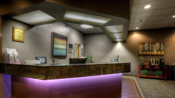 A reception area with a marble counter, ceiling lights, framed certificates, and a decorative wall piece. - Royal Hotel (Lloydminster)