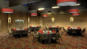 A conference room with multiple round tables, each set with chairs and red napkins. - Royal Hotel (Lloydminster)