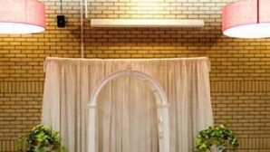 A venue with a brick wall, a white archway, and rows of chairs with white covers and red sashes. - Royal Hotel (Lloydminster)