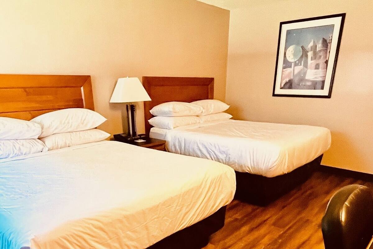 A hotel room with two beds, a nightstand, a lamp, and a framed picture on the wall.