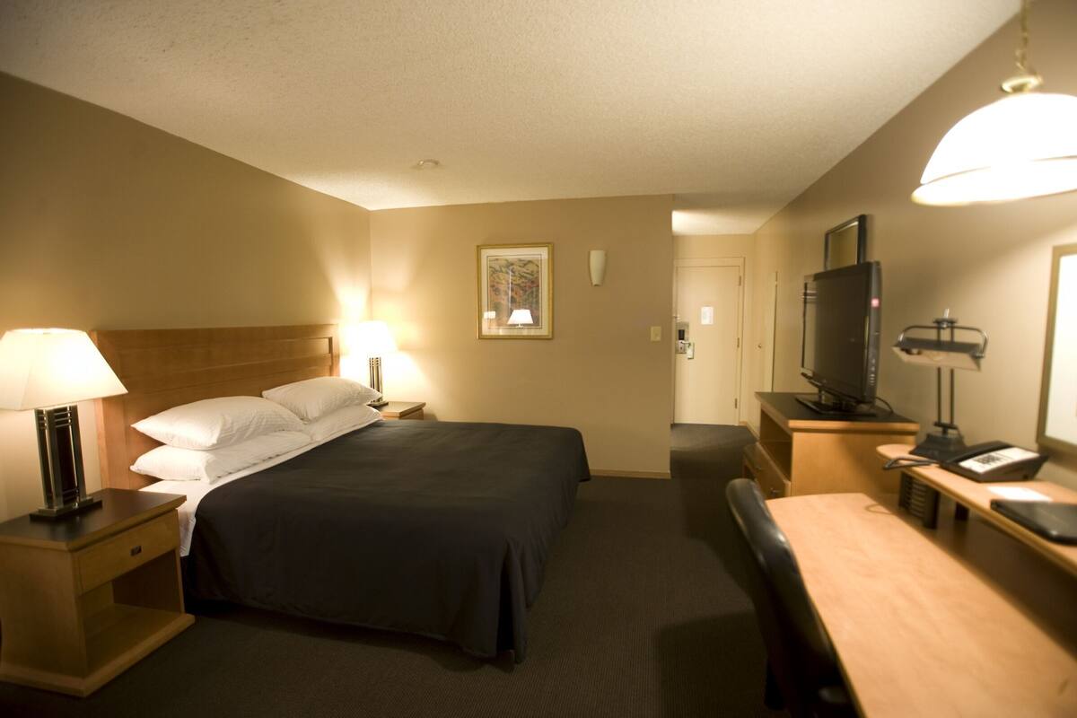 A hotel room with a bed, bedside tables with lamps, a desk with a chair, a television, and a door.