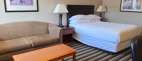 Habitación de hotel con cama, sofá, mesita de noche, lámpara y un cuadro en la pared.