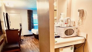 A hotel room with a wooden floor, a desk with a chair, a bed, a microwave, a hairdryer, and a mirror with lights. - Royal Hotel (Lloydminster)
