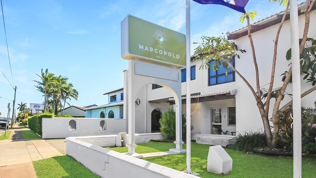 Entrada de hotel con un letrero que dice "The Marco Polo Hotel", una bandera y un césped bien cuidado.