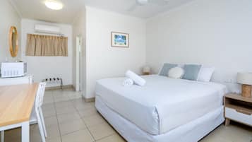 Una habitación de hotel con una cama, un escritorio, una silla, un ventilador de techo, un equipo de aire acondicionado y un cuadro en la pared.