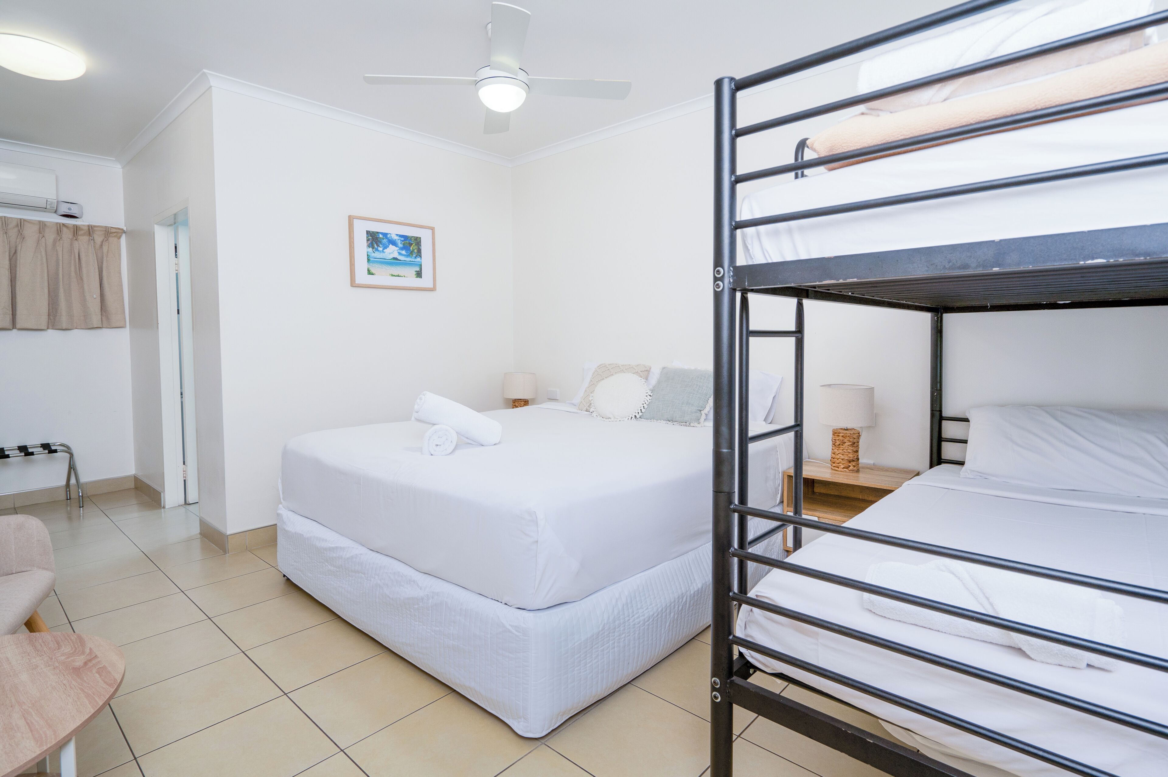 Habitación con literas, ventilador de techo, mesita de noche con lámpara y un cuadro en la pared.