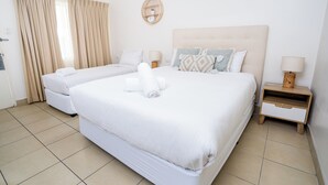 Habitación de hotel con dos camas, una mesita de noche con lámpara, estante en la pared y ventana con cortinas.