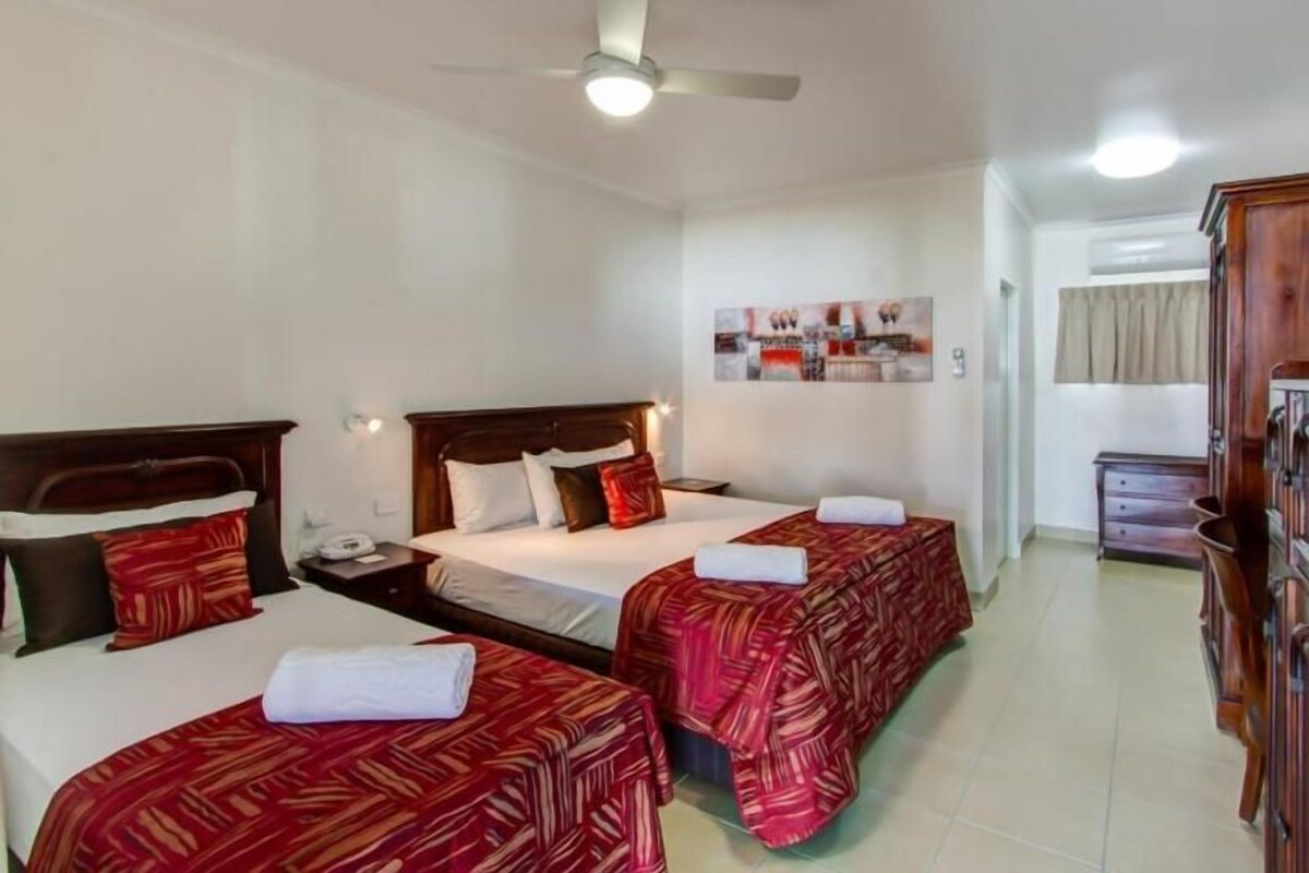 A hotel room with two beds, a ceiling fan, a nightstand, a bedside table, and a mirror.