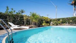Piscina azul cristalina con una tumbona blanca y una escalera metálica.