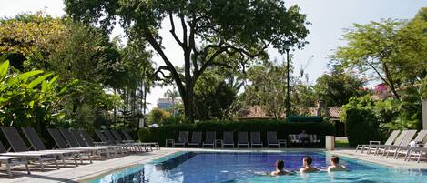 A swimming pool with lounge chairs and a large tree in the background.