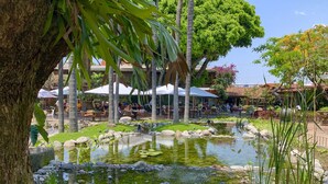 Un jardín tranquilo con un estanque, zonas de estar y sombrillas.