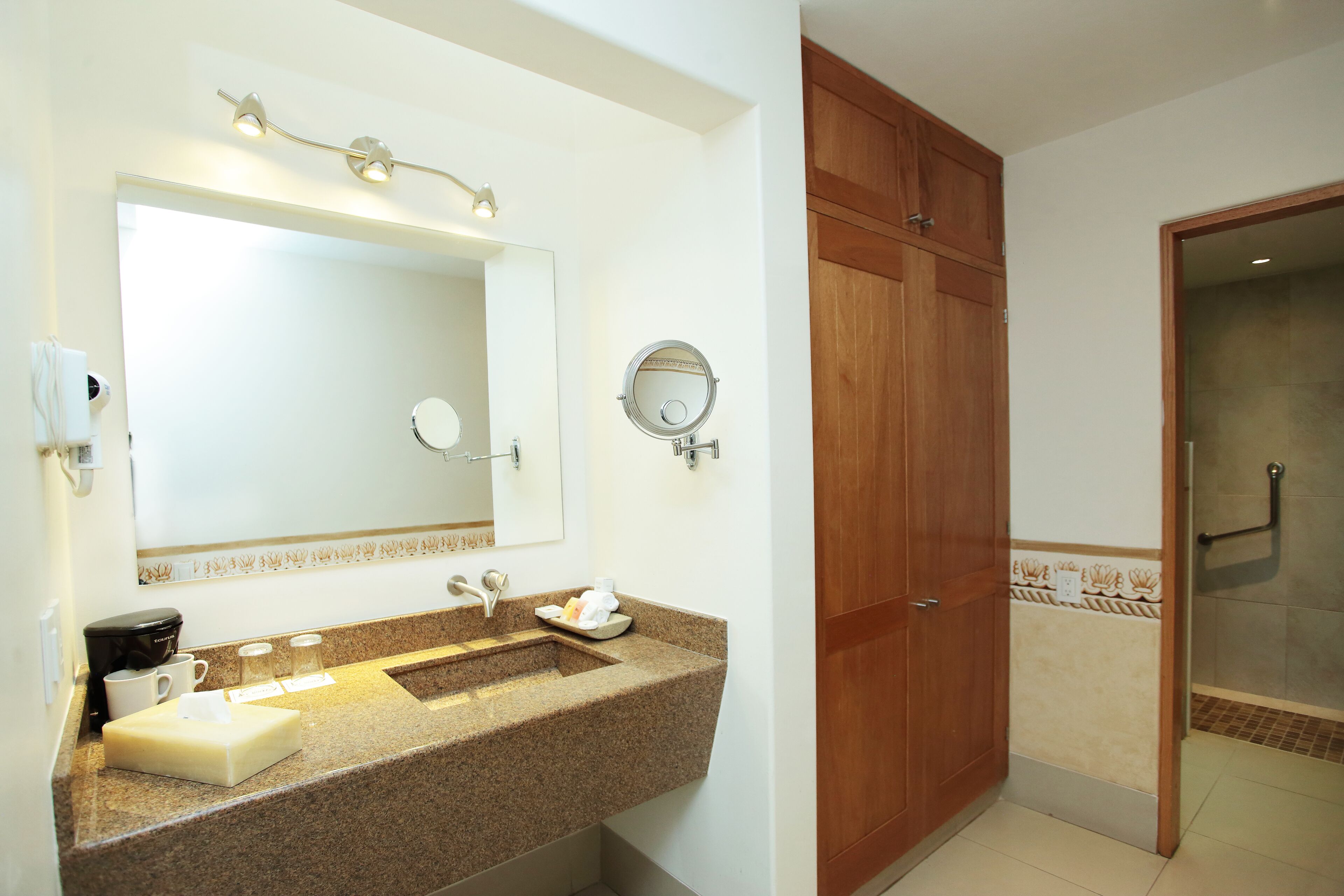 A bathroom with a granite countertop, a large mirror, a wooden cabinet, and a shower area.