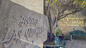 Un letrero de piedra con la inscripción "Hosteria las Quintas", un banco verde y un árbol con hojas.