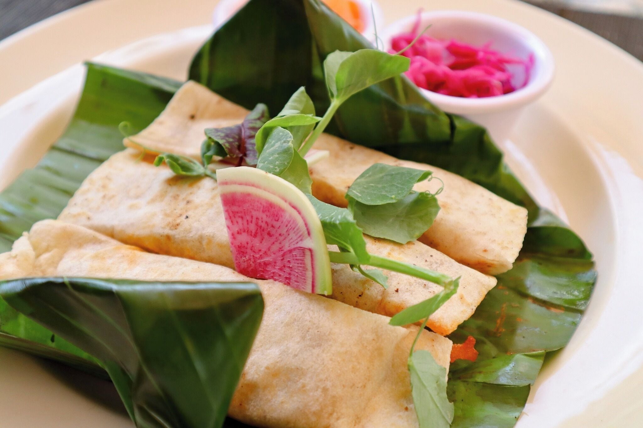 A plate of food with wraps, greens, and a small bowl of sauce.