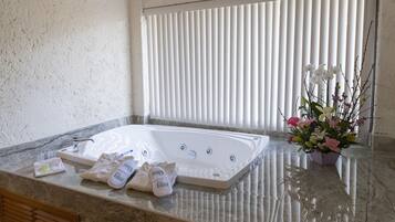 A bathroom with a large bathtub, a marble countertop, a towel rack, and a potted plant.