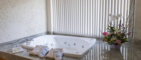 A bathroom with a large bathtub, a marble countertop, a towel rack, and a potted plant.