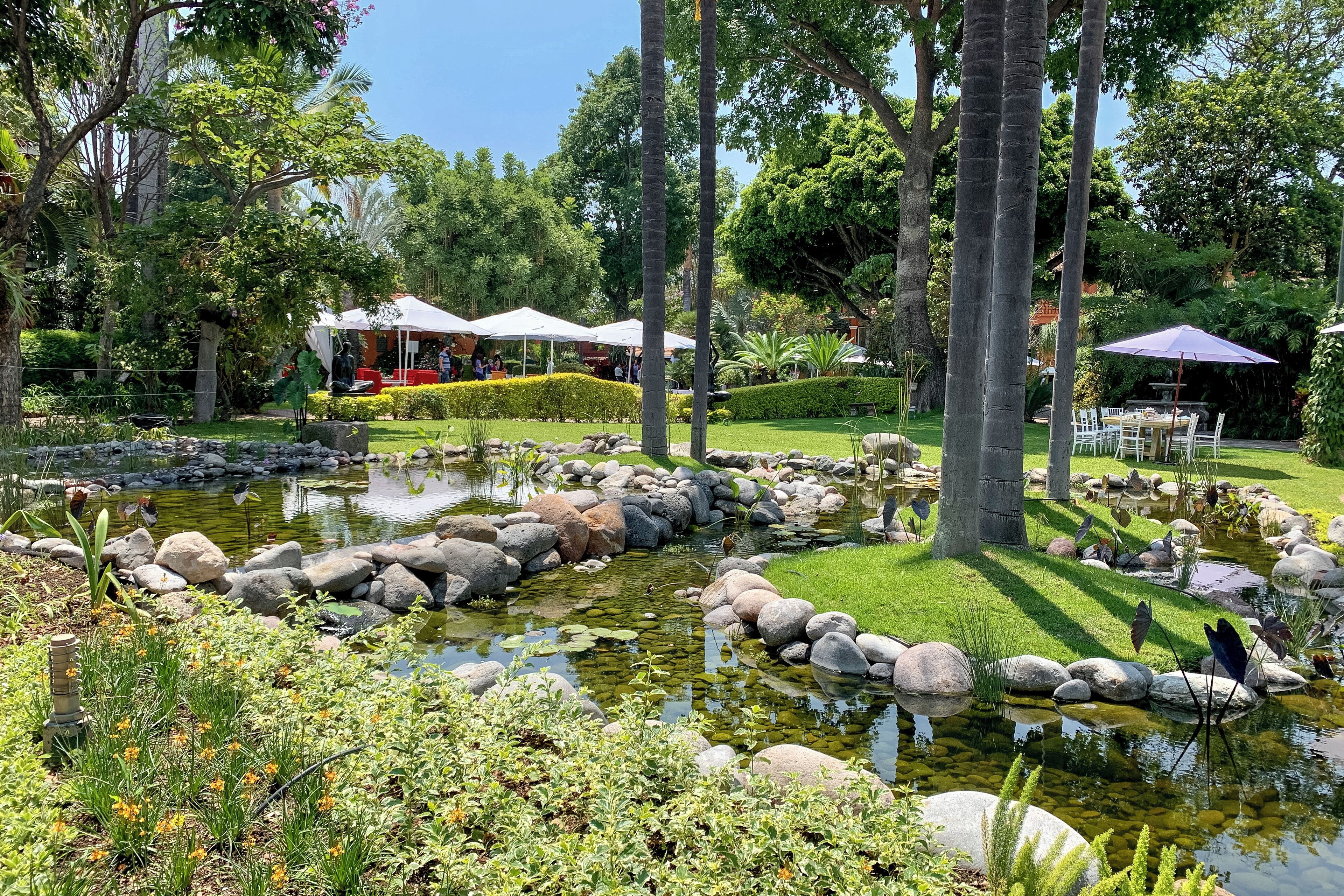 A garden with a pond, rocks, and a dining area with umbrellas.
