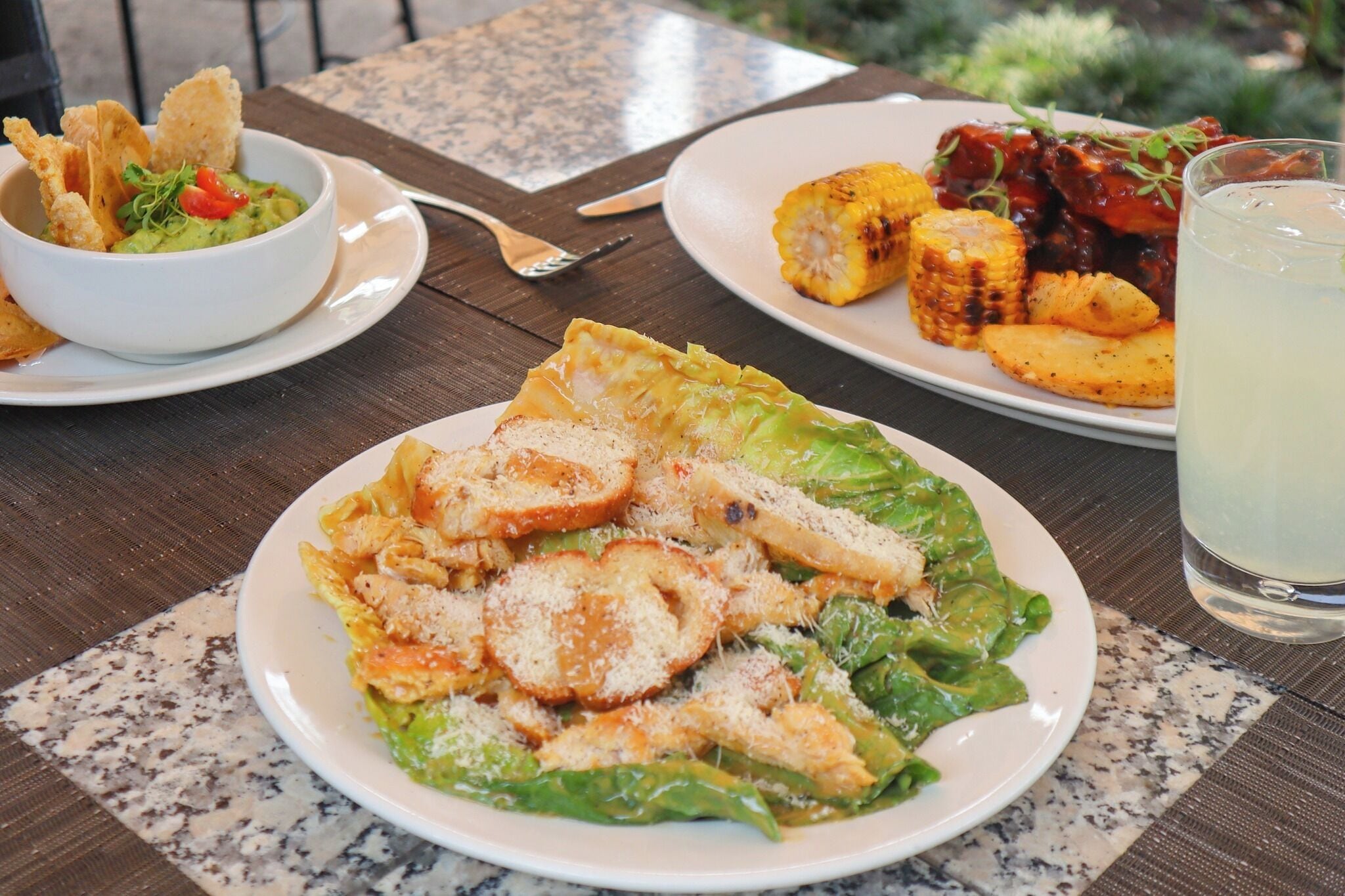 A table with plates of food including a salad, corn on the cob, and a bowl of guacamole.
