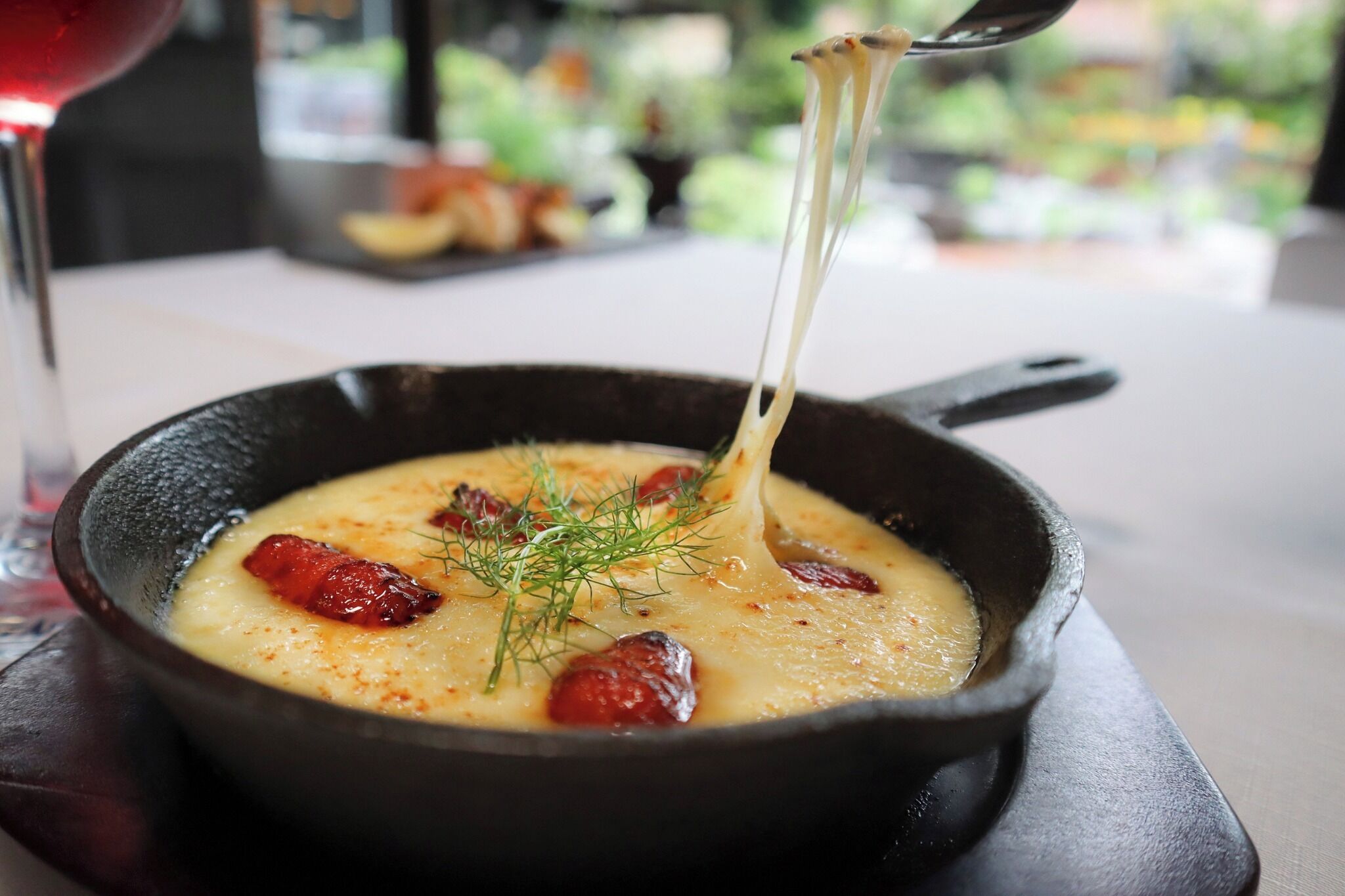 A close-up of a creamy dish with cheese stretching, garnished with herbs, served in a black skillet.