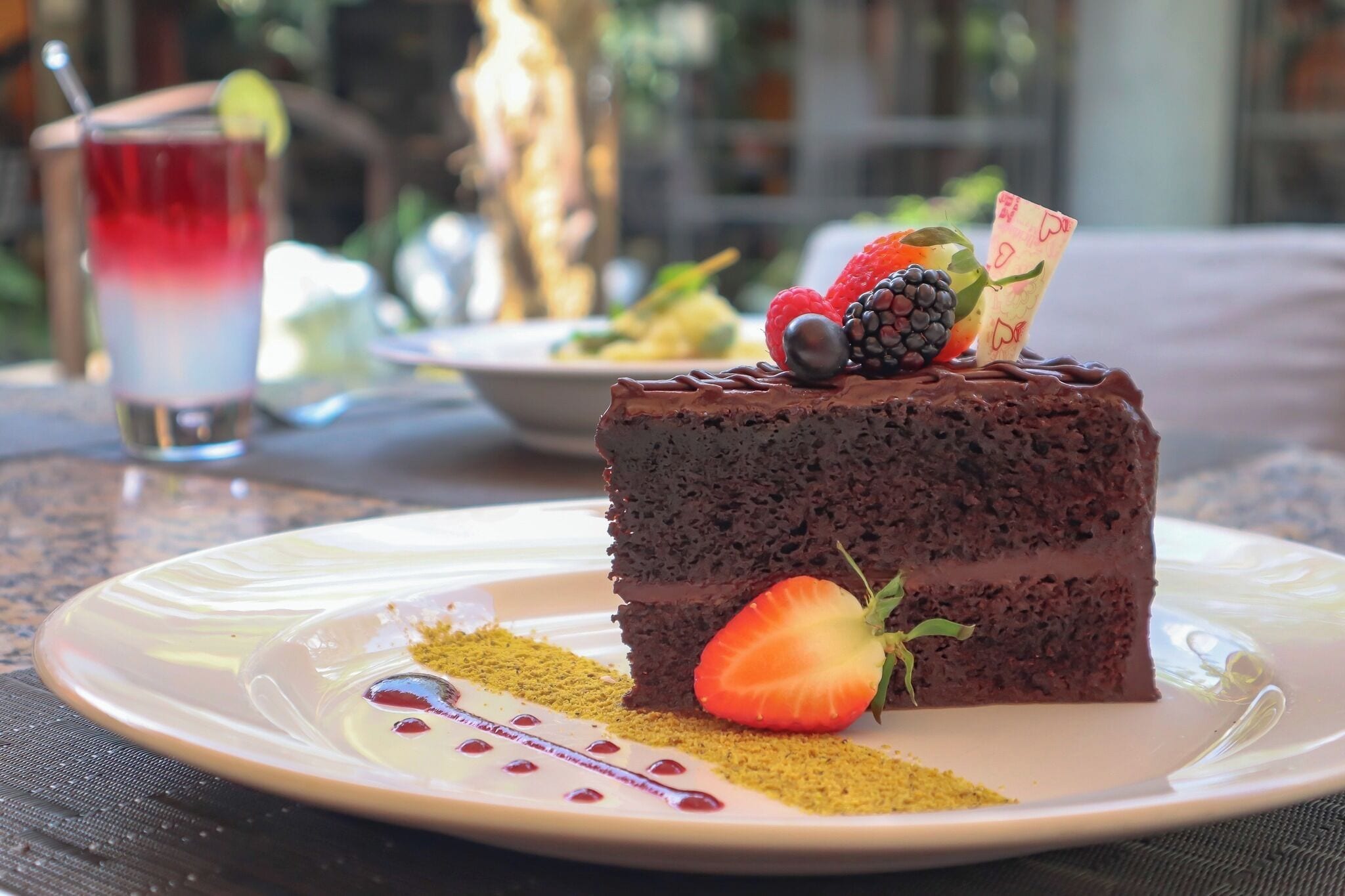 Una porción de pastel de chocolate con fresas y una mora sobre un plato blanco.