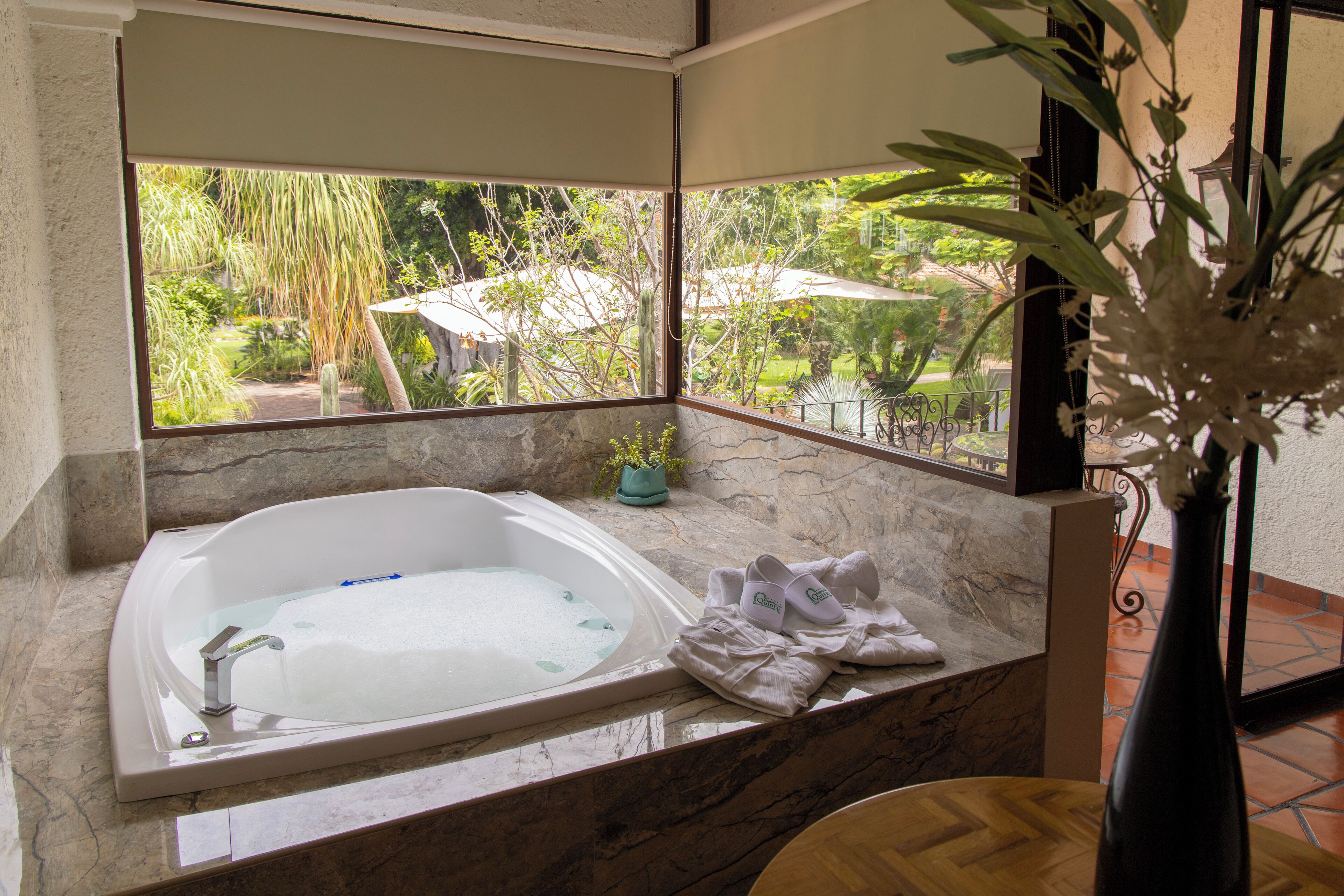 A bathroom with a large bathtub, a view of a garden, and a vase with flowers.