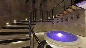 Un interior moderno con una pared de piedra, una fuente central y una escalera con barandillas de metal.