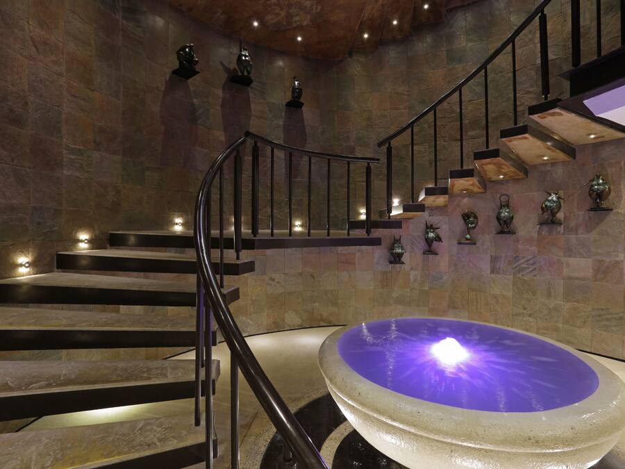 Un interior moderno con una pared de piedra, una fuente central y una escalera con barandillas de metal.