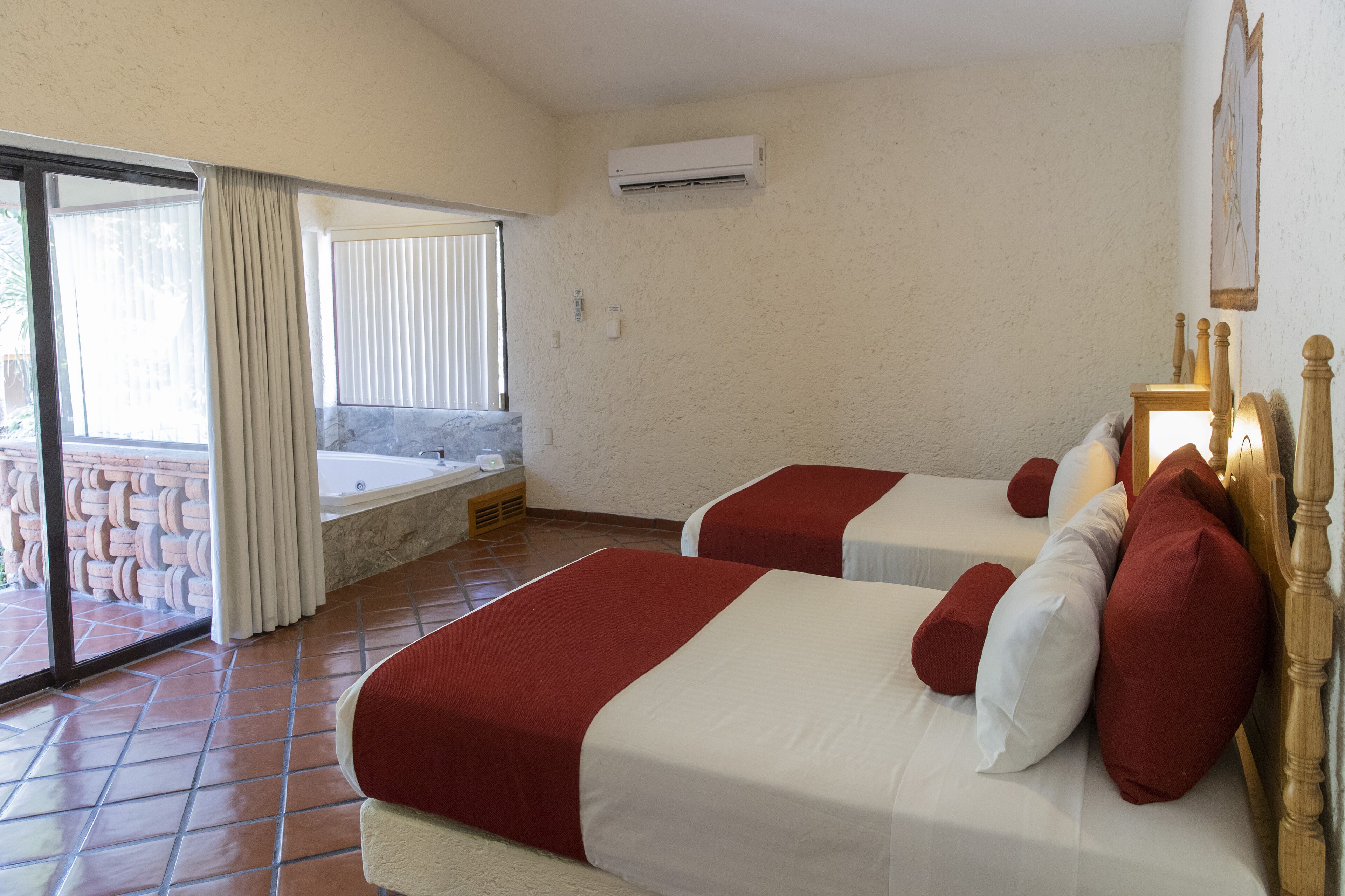 A hotel room with two beds, a bathtub, and a sliding glass door to a balcony.